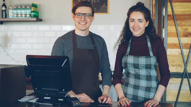 Dois empreendedores sorrindo atrás do balcão do próprio negócio